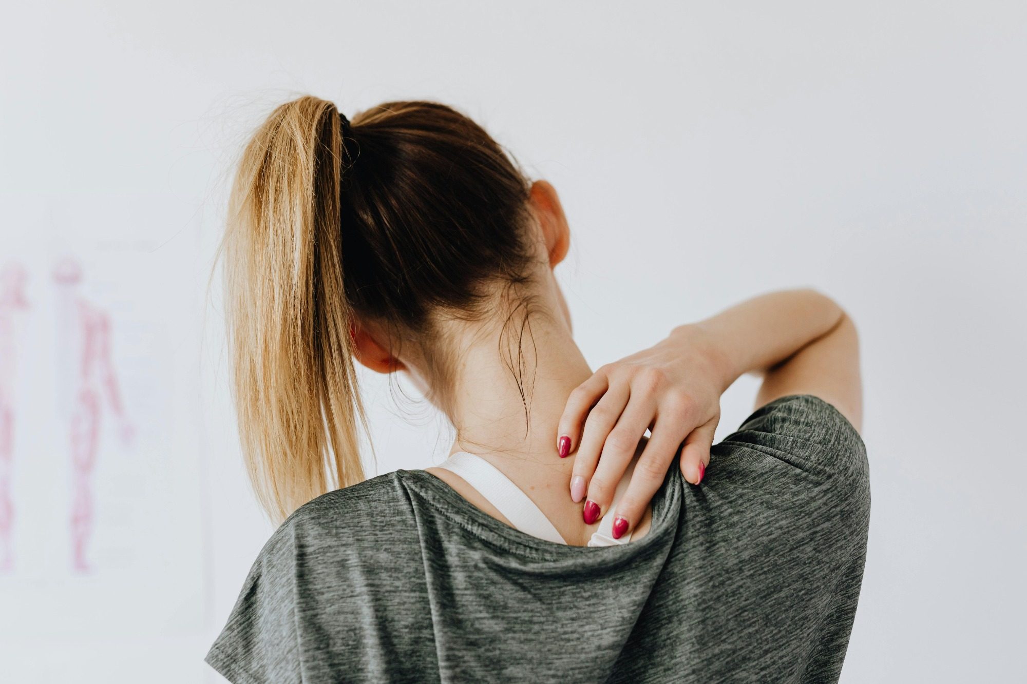 Image of a woman reaching behind her head and touching her neck indicating that she's in pain